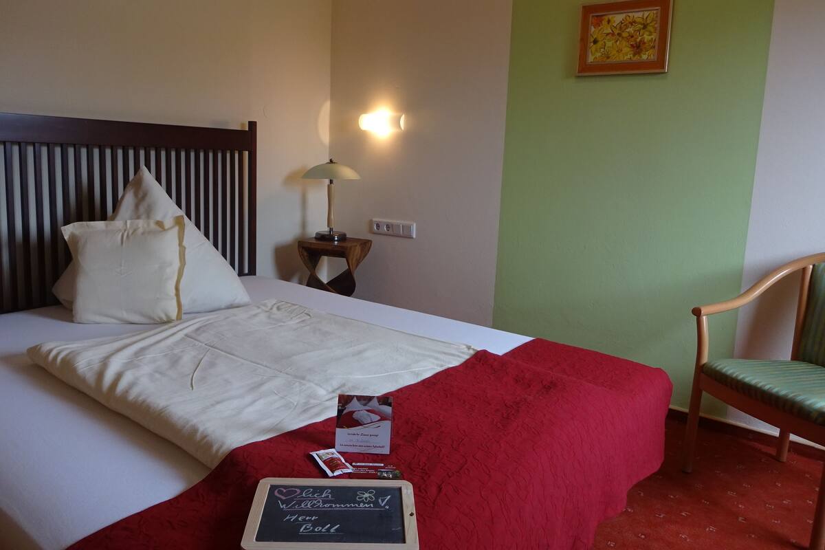 A neatly made bed with a red blanket, a bedside lamp, and a framed picture on the wall.