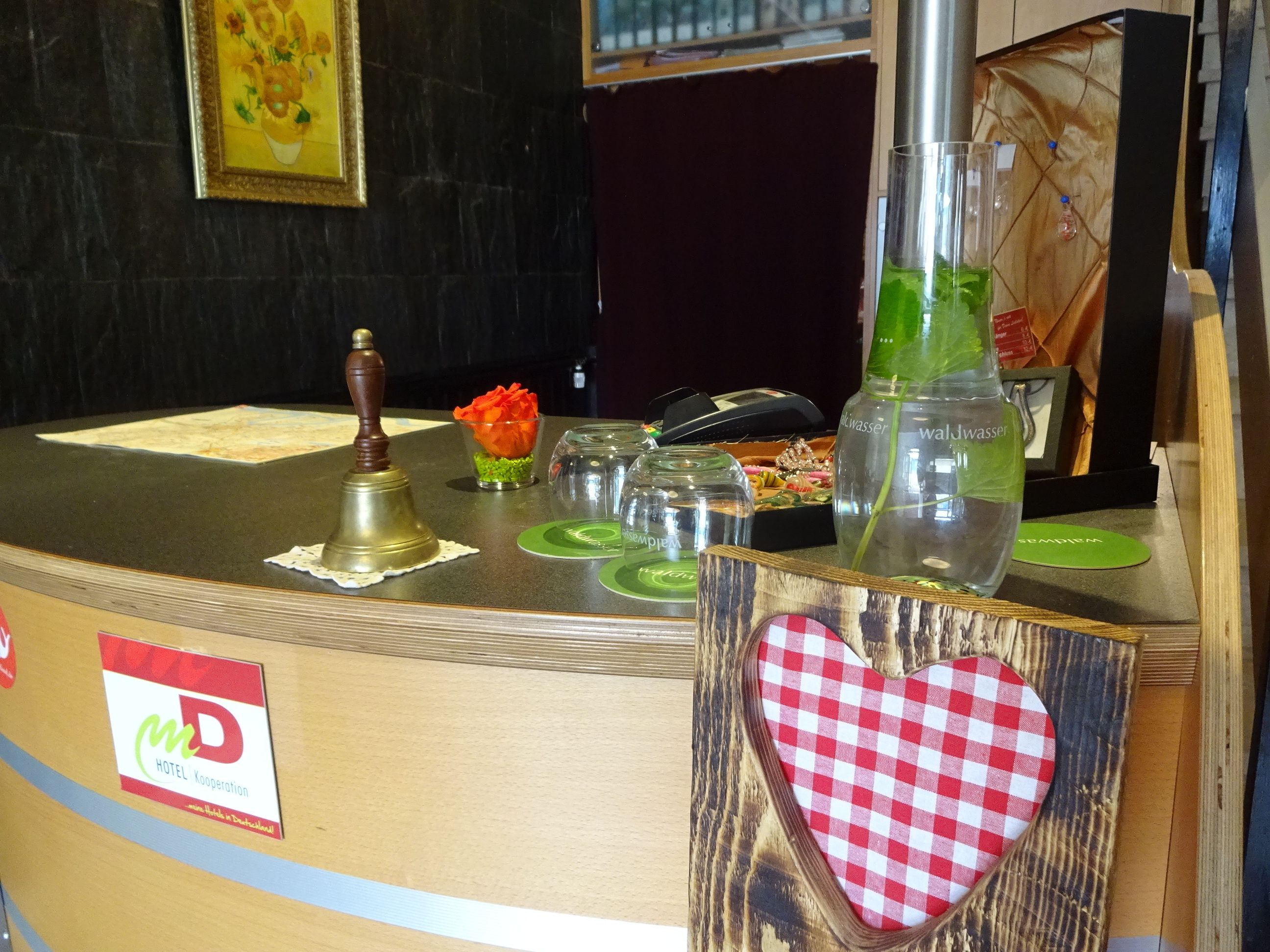 A hotel reception desk with a wooden counter, a bell, a flower vase, and a heart-shaped decoration.