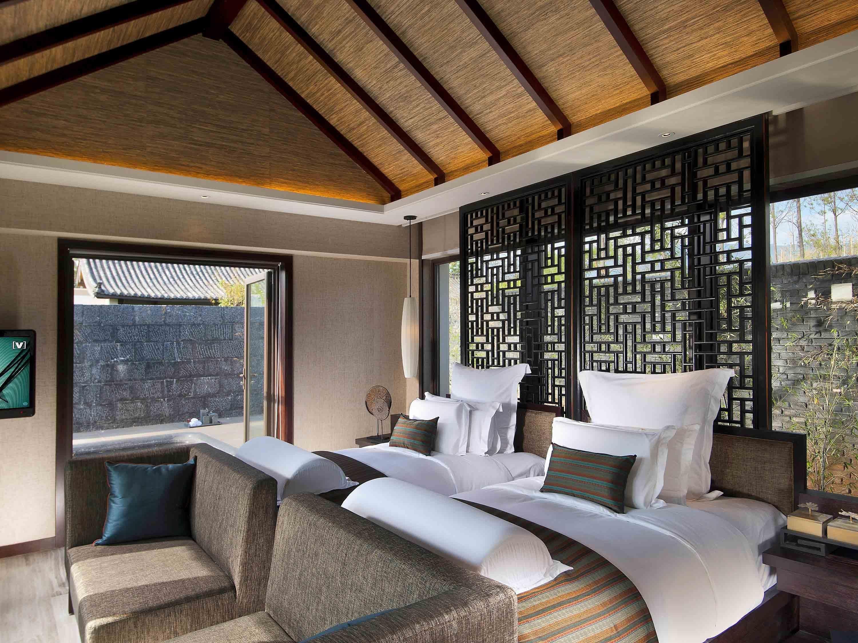 Habitación de hotel moderna con una cama grande, un sofá, un biombo decorativo y vistas al exterior.