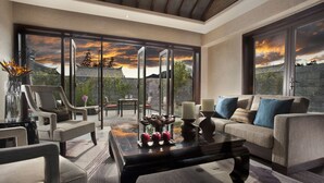 A modern living room with a sofa, chairs, and a coffee table. There is a large window with a view of traditional architecture and a sunset. - Pullman Lijiang Resort and Spa (Lijiang)