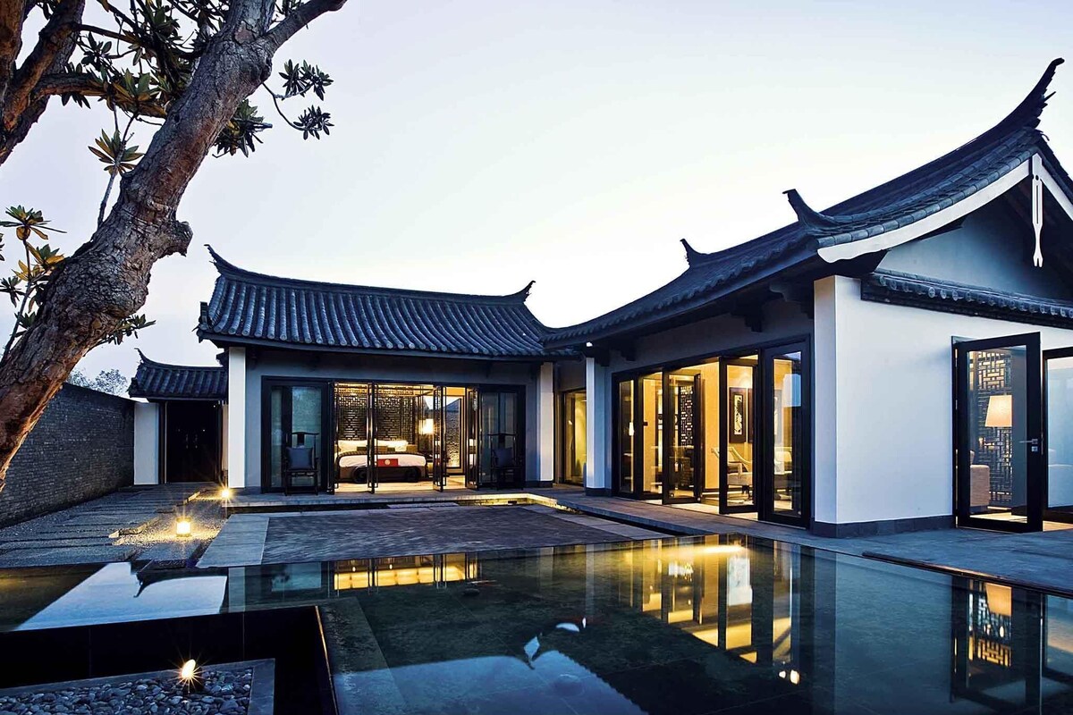 A traditional-style building with a reflective pool, large glass doors, and a modern interior visible through the doors.