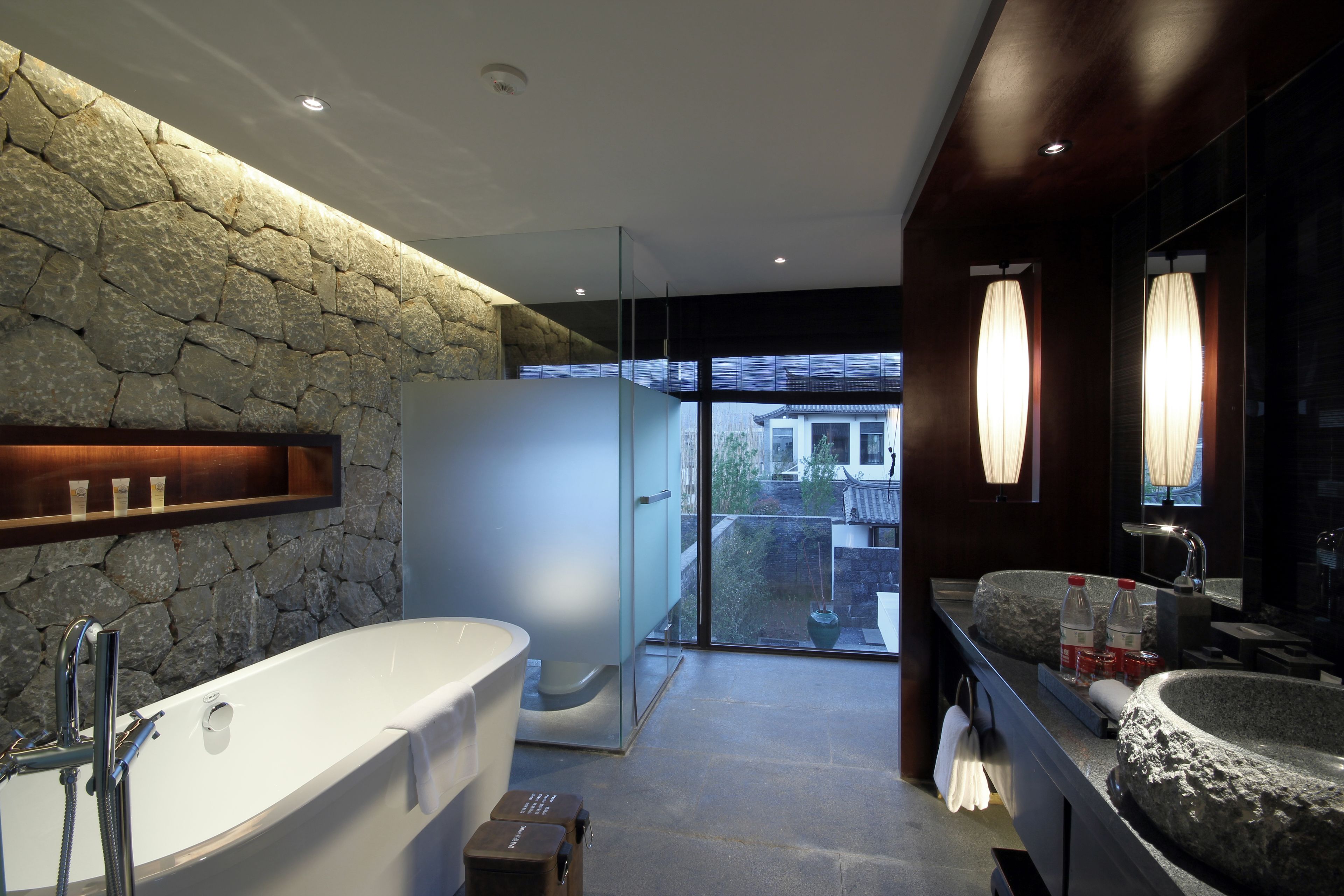 Un baño moderno con pared de piedra, una bañera grande, una ducha con cerramiento de vidrio y un lavabo con recipiente de piedra.