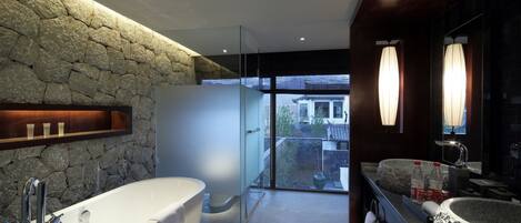 Un baño moderno con pared de piedra, una bañera grande, una ducha con cerramiento de vidrio y un lavabo con recipiente de piedra.