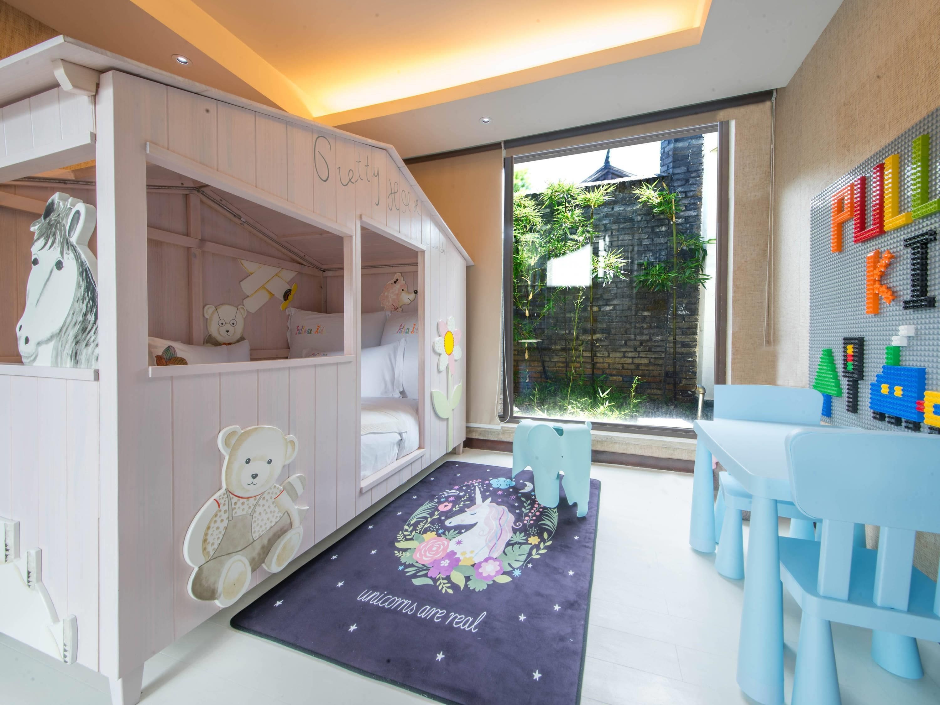 A children's playroom with a pink bunk bed, a bear-themed rug, and a LEGO wall.