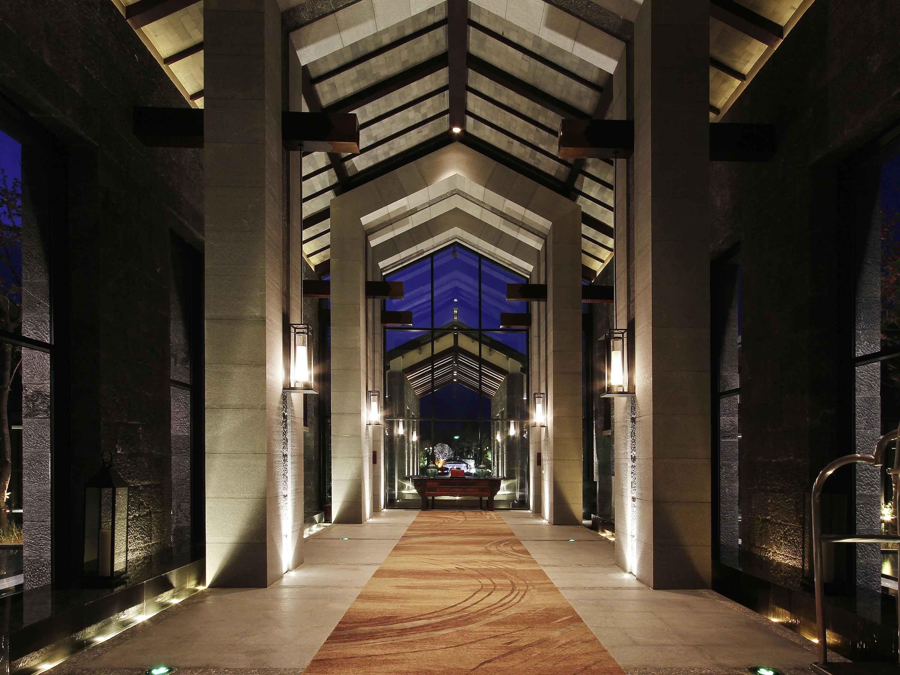 A hotel lobby with a central corridor, stone columns, and a patterned carpet.