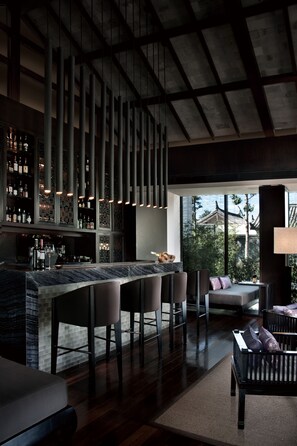 A modern bar area with a high ceiling, a bar counter with stools, and a seating area with a sofa and chairs. - Pullman Lijiang Resort and Spa (Lijiang)