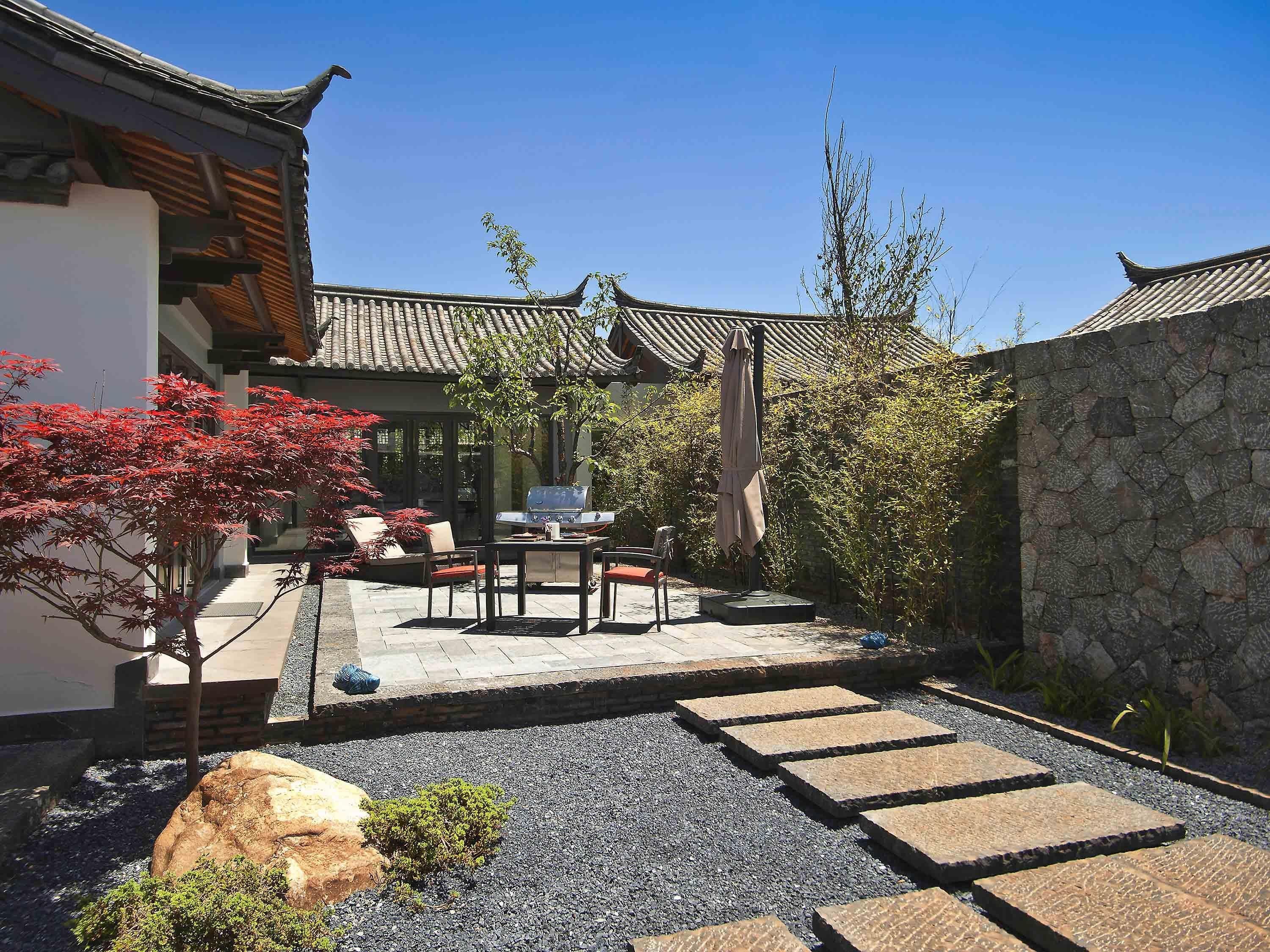A traditional Japanese-style courtyard with a stone wall, a tiled roof, and a seating area with a table and chairs.