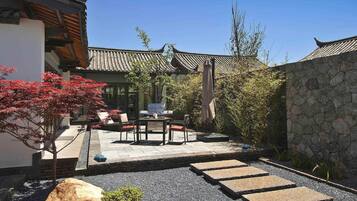 A traditional Japanese-style courtyard with a stone wall, a tiled roof, and a seating area with a table and chairs.