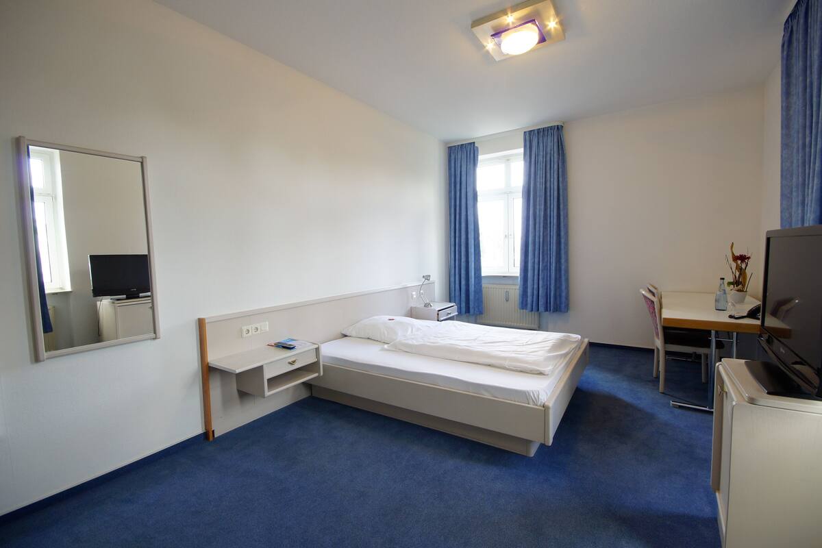 A hotel room with a bed, a desk, a chair, a TV, and a window with curtains.