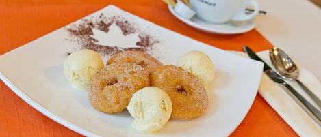 A plate with doughnuts and ice cream, a cup of coffee, and a spoon on an orange tablecloth.
