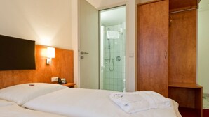 Habitación de hotel con una cama grande, un armario de madera, zona de ducha y teléfono junto a la cama.