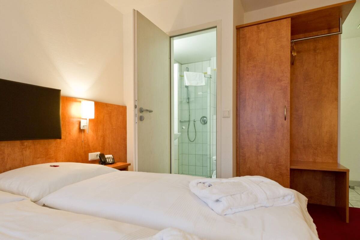A hotel room with a large bed, a wooden wardrobe, a shower area, and a bedside telephone.