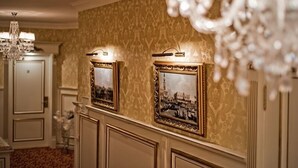 A hallway with ornate wallpaper, framed pictures, and a chandelier. - Royal City Hotel (Kyiv)