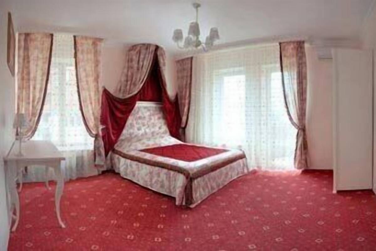 A bedroom with a bed, curtains, a chandelier, and a red carpet.
