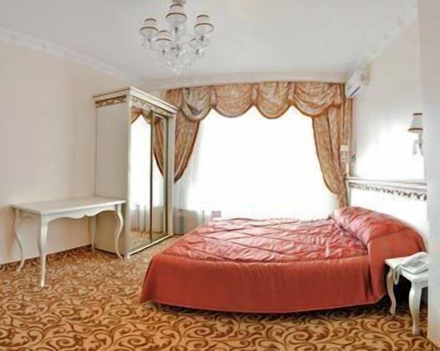 A bedroom with a large bed, a wardrobe, a desk, and a chandelier.
