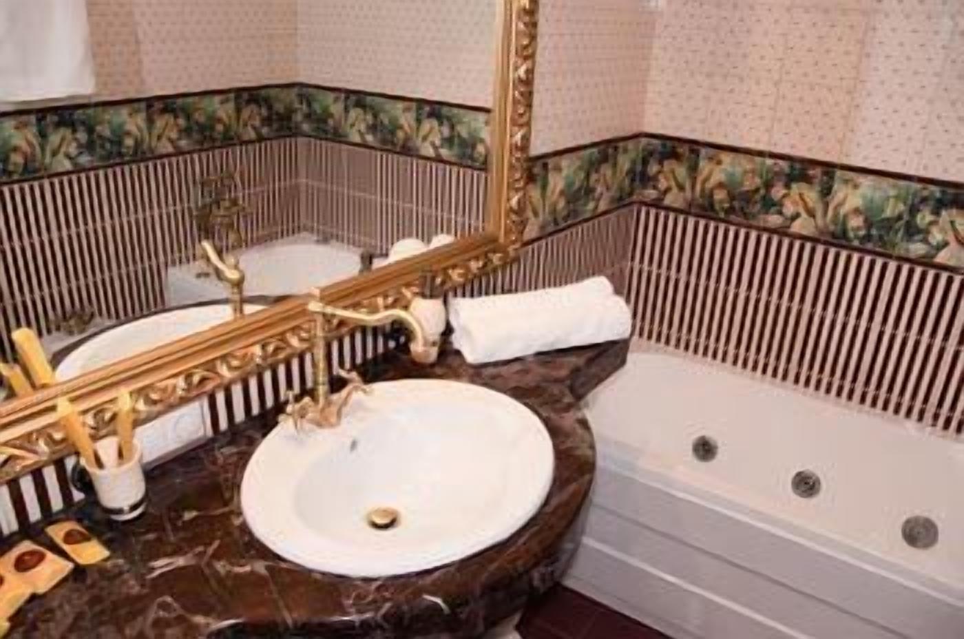 A bathroom with a marble sink, a bathtub, and a mirror with a decorative frame.