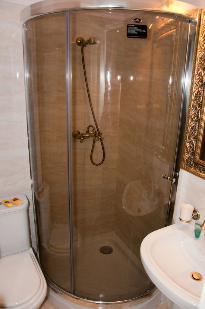 A glass-enclosed shower stall with a handheld showerhead, a toilet, and a sink with a mirror.