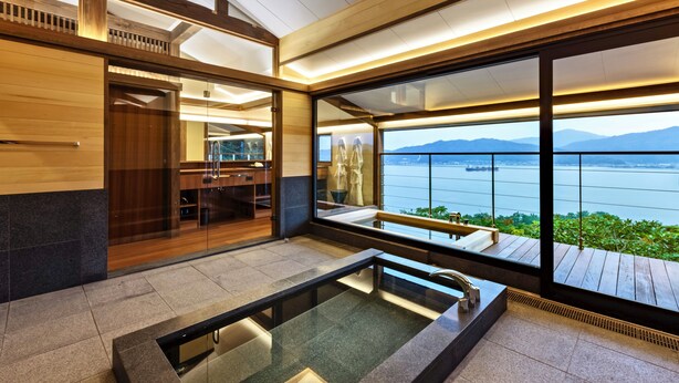 A modern bathroom with a glass-enclosed shower, a wooden vanity, and a large window offering a view of a lake and mountains. - Genmyoan (Miyazu)