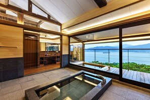 A modern bathroom with a glass-enclosed shower, a wooden vanity, and a large window offering a view of a lake and mountains.