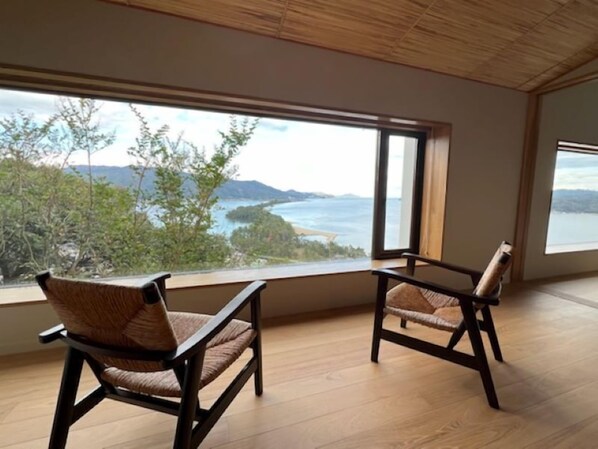 A room with two wicker chairs facing a large window overlooking a coastal landscape.