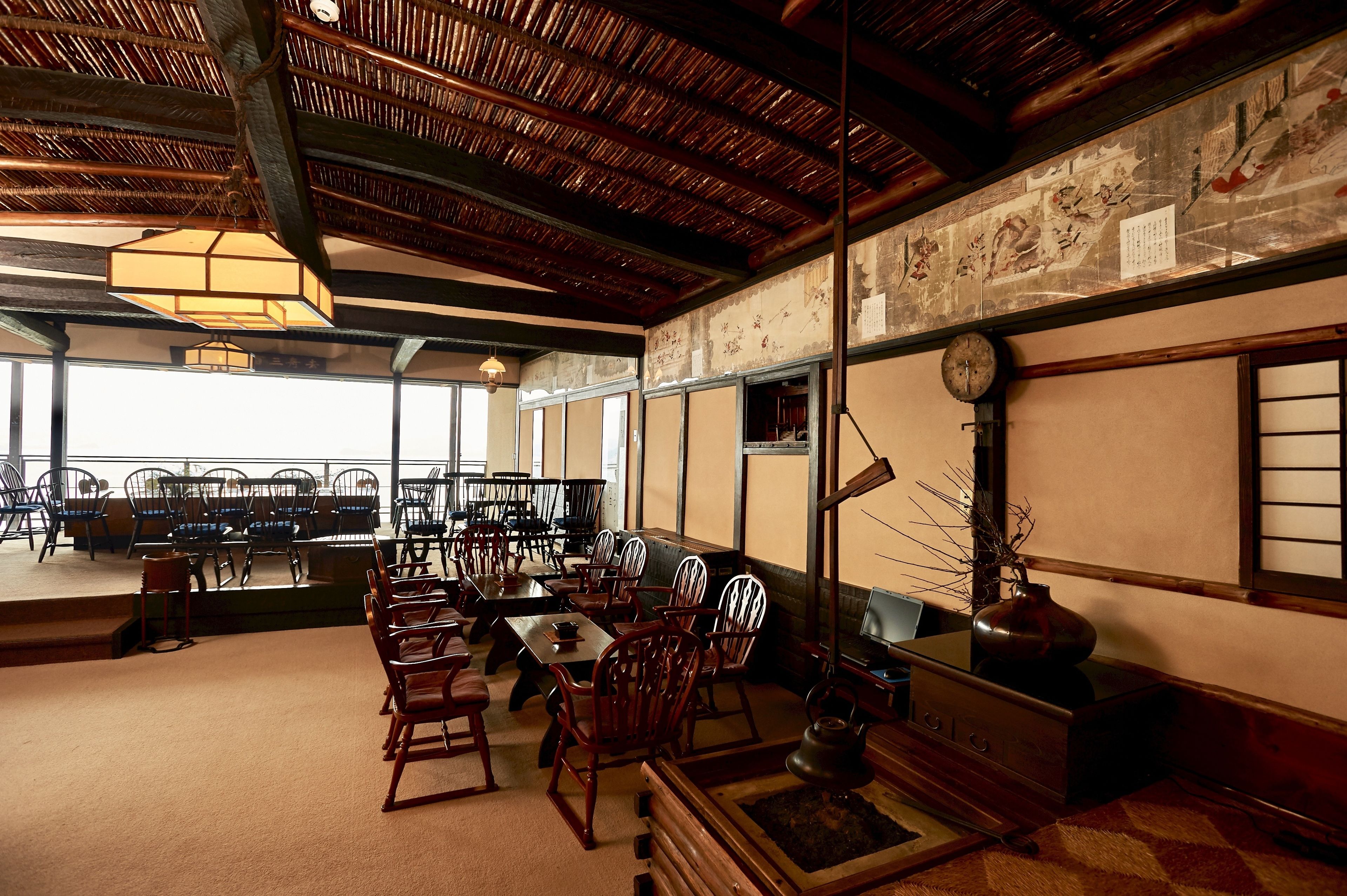 A traditional Japanese-style dining room with tatami mats, wooden furniture, and a high ceiling with exposed beams.