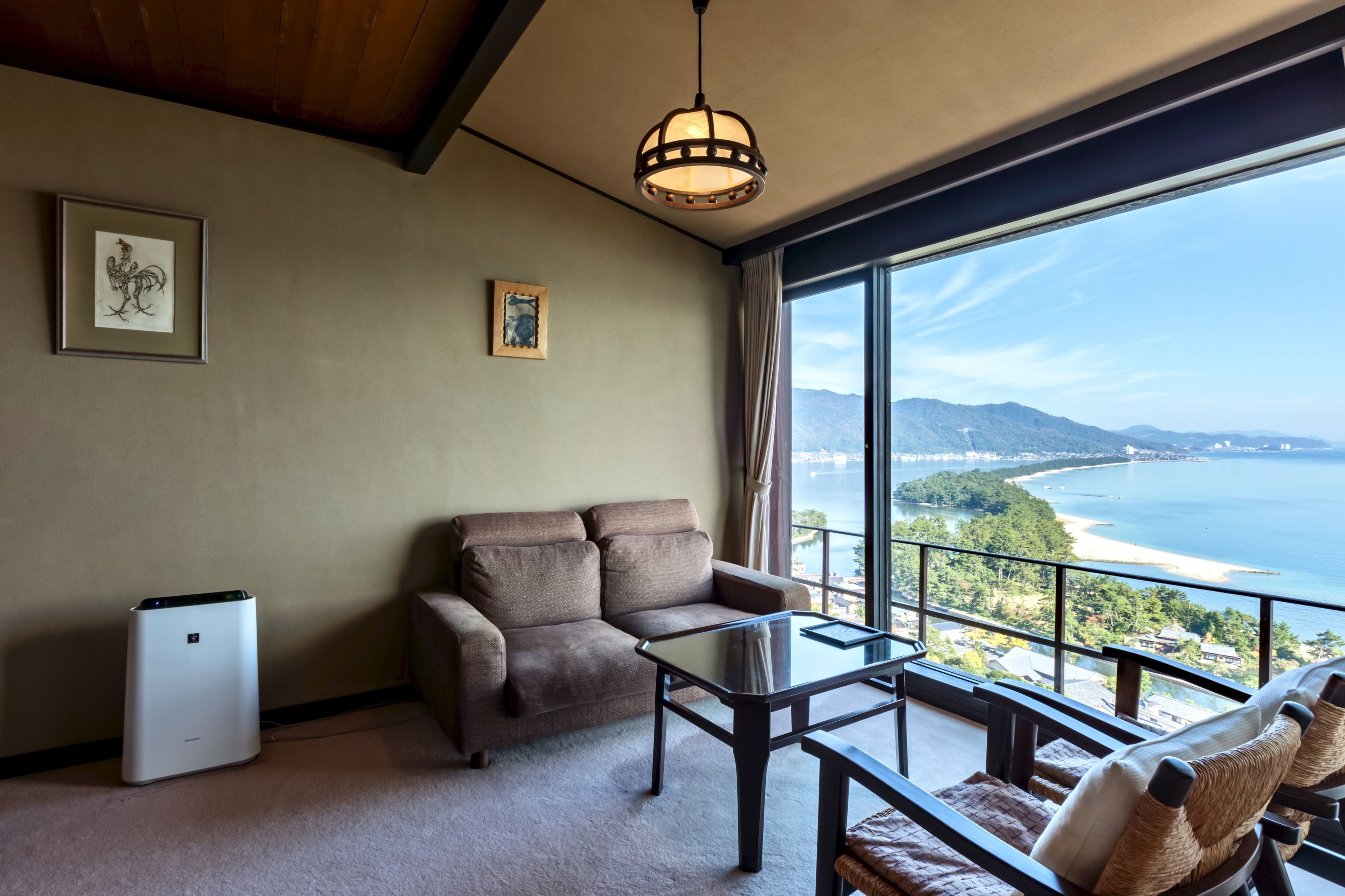 A room with a sofa, a small table, a white appliance, and a view of the ocean.