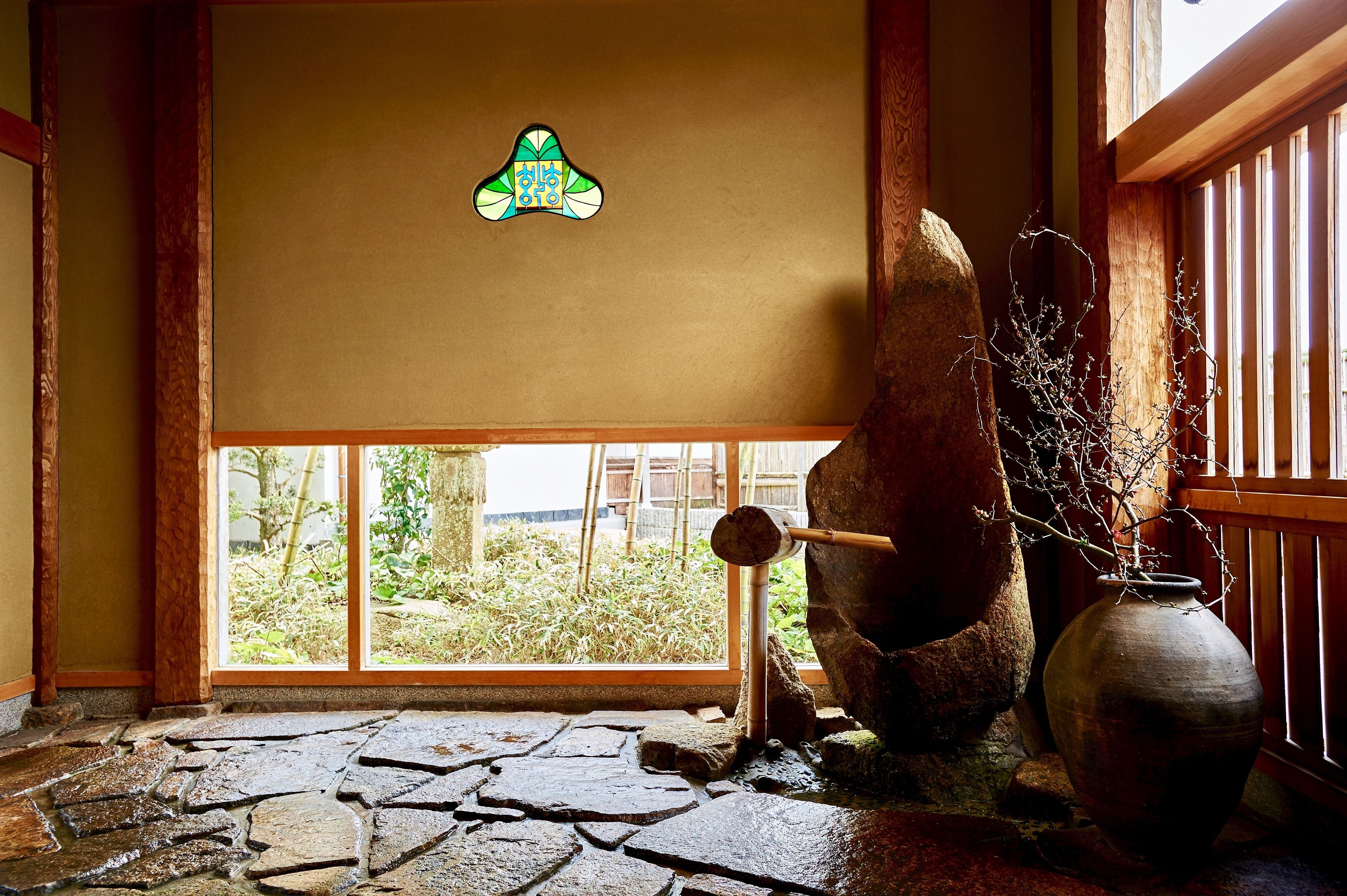 A stone-tiled floor, a wooden beam, a large rock, and a vase with branches.