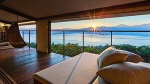 A modern room with a large window overlooking a body of water and mountains. There is a bed with pillows and a hanging chair. - Genmyoan (Miyazu)