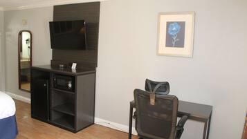 A hotel room with a bed, a desk with a chair, a television, a microwave, and a framed picture on the wall.