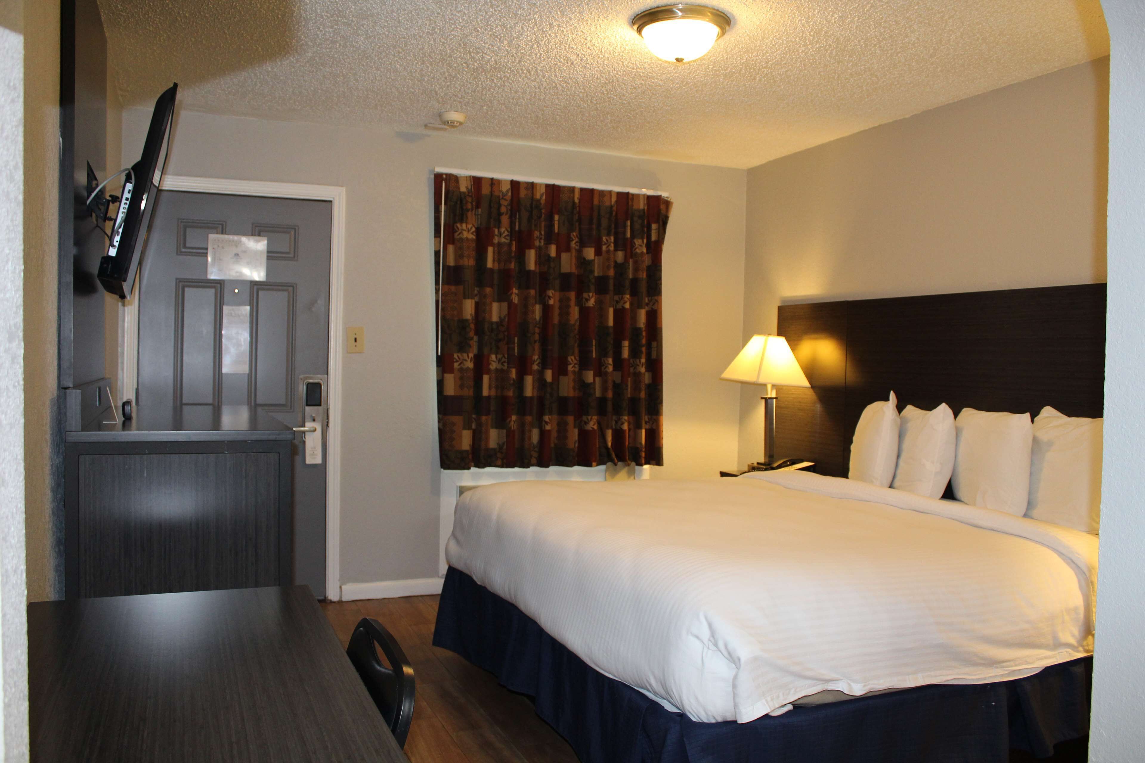 A hotel room with a bed, a desk, a television mounted on the wall, and a window with curtains.