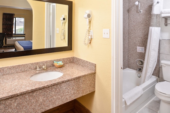 A bathroom with a granite countertop sink, a hairdryer mounted on the wall, a bathtub, and a toilet.