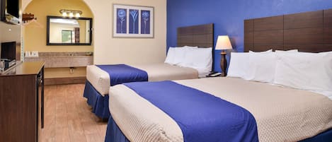 A hotel room with two beds, a desk, a mirror, and a bathroom vanity.