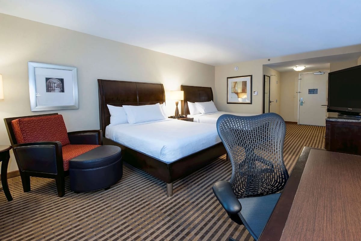 Ein Hotelzimmer mit einem großen Bett, zwei Nachttischen, einem Fernseher, einem Sessel und einem Schreibtisch.