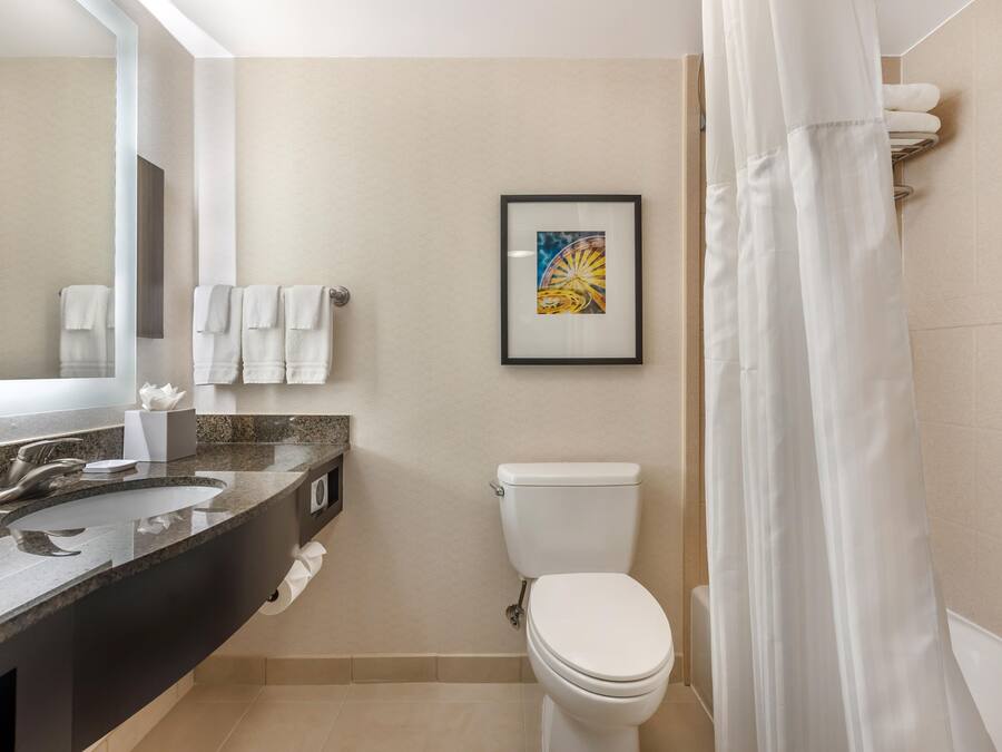 A modern bathroom with a granite countertop, a white toilet, and a framed picture on the wall.