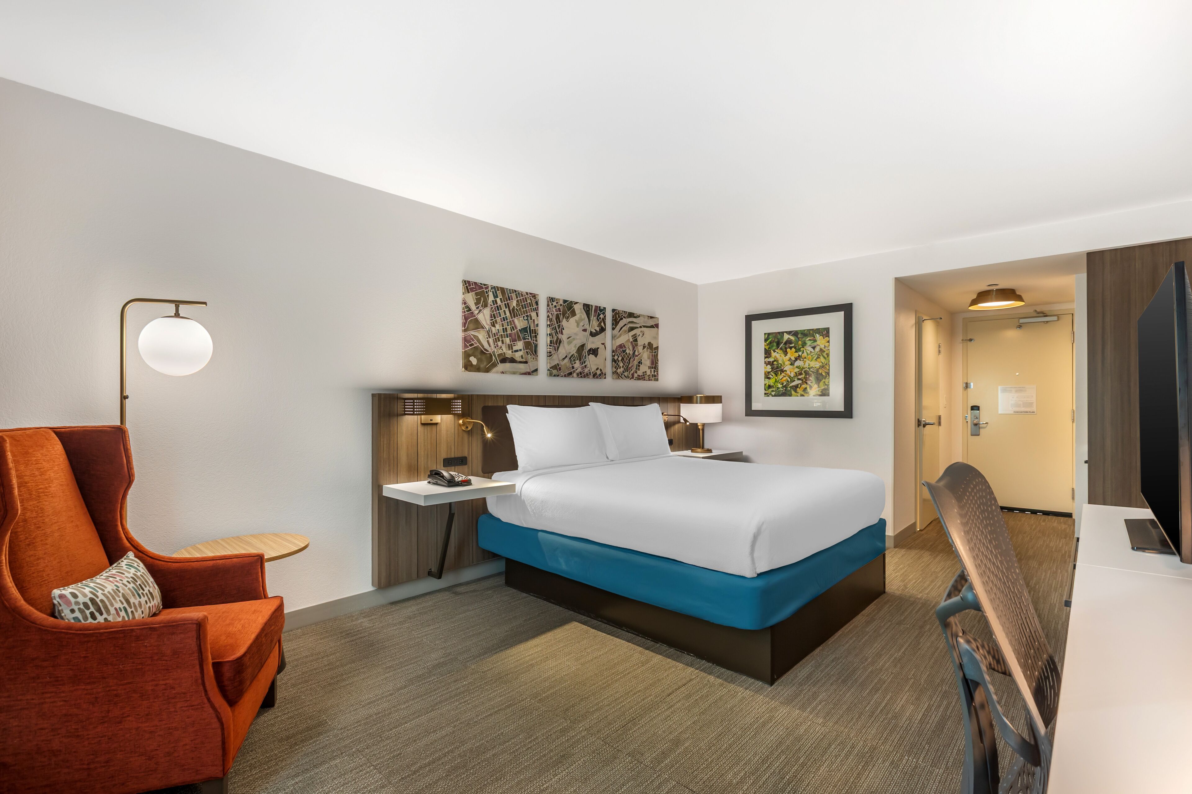 Una habitación de hotel con cama, escritorio, silla y mesita de noche.