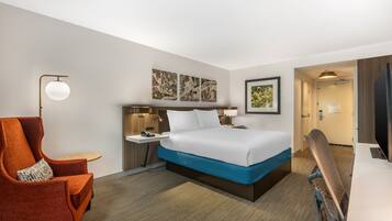 Una habitación de hotel con cama, escritorio, silla y mesita de noche.