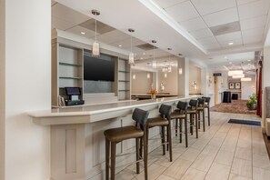 A modern bar area with a long counter, multiple bar stools, and pendant lighting. - Hilton Garden Inn Columbia Northeast (Columbia)