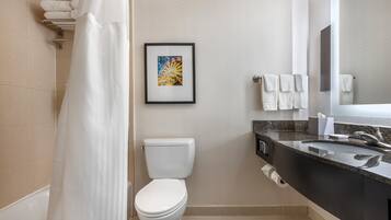 Un baño moderno con cortina de ducha, inodoro, obra de arte enmarco, toallas y lavamanos con espejo.