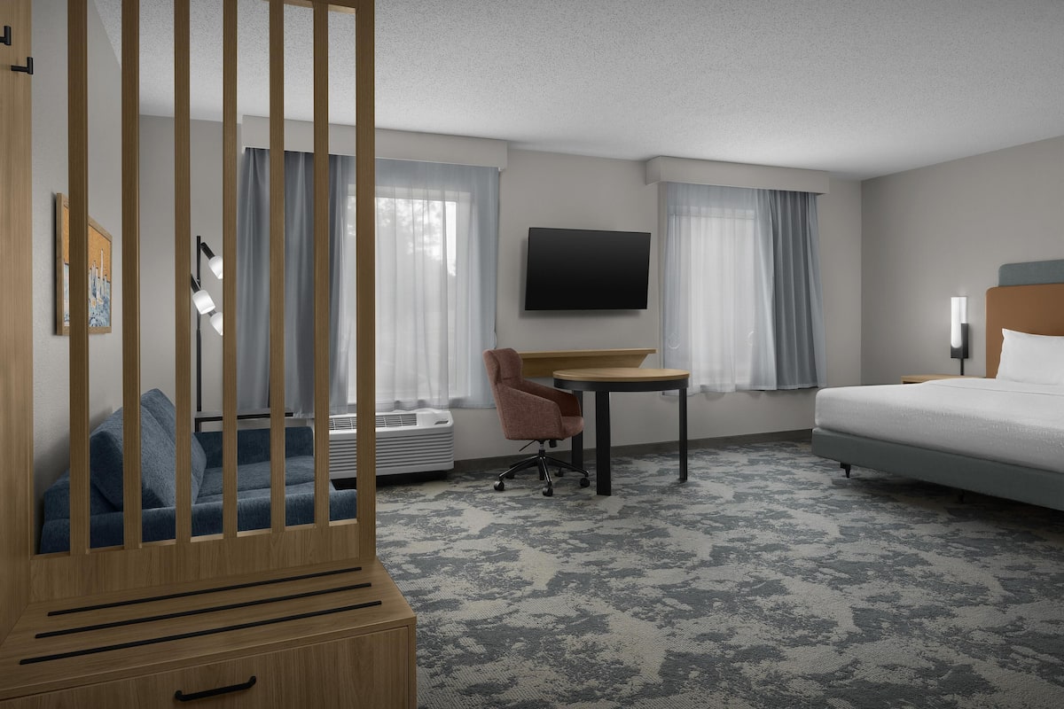 A hotel room with a bed, a desk, a chair, a TV, and a window with curtains.