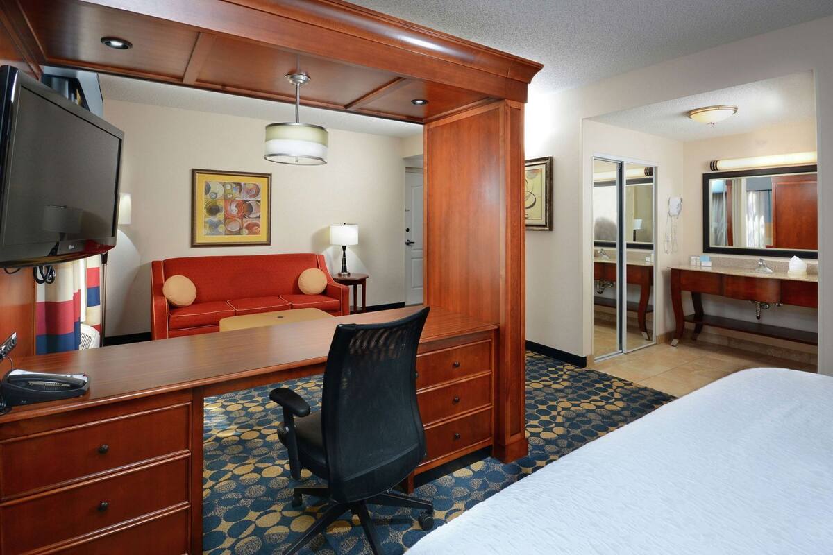 A hotel room with a bed, desk, chair, television, and a bathroom with a mirror and sink.