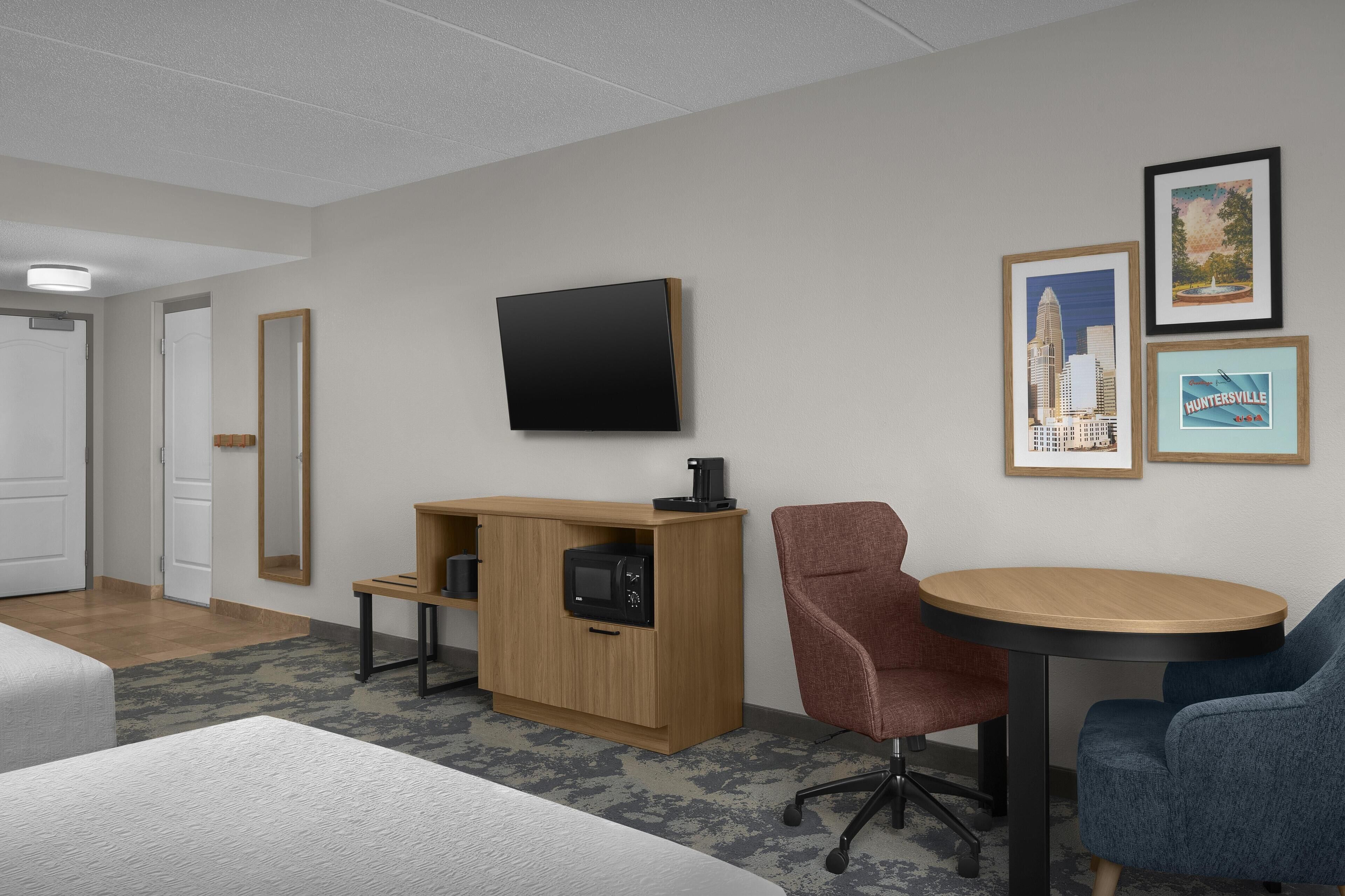 A hotel room with a bed, a desk with a computer, a TV, and framed pictures on the wall.