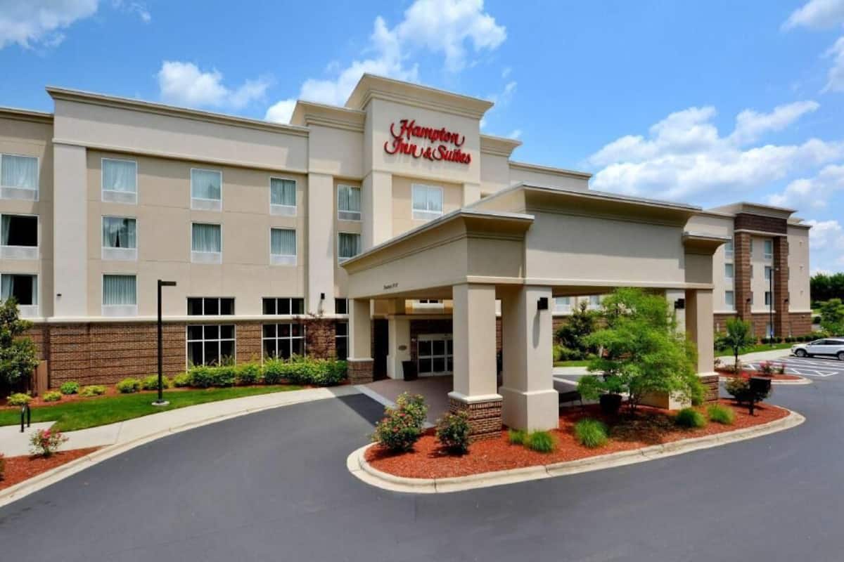 A Hampton Inn & Suites hotel with a modern facade, a covered entrance, and landscaped grounds.