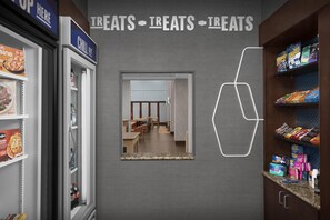 A grocery store with a freezer section on the left, a mirror reflecting the interior, and shelves stocked with snacks and beverages on the right. - Hampton Inn & Suites Huntersville (Huntersville)