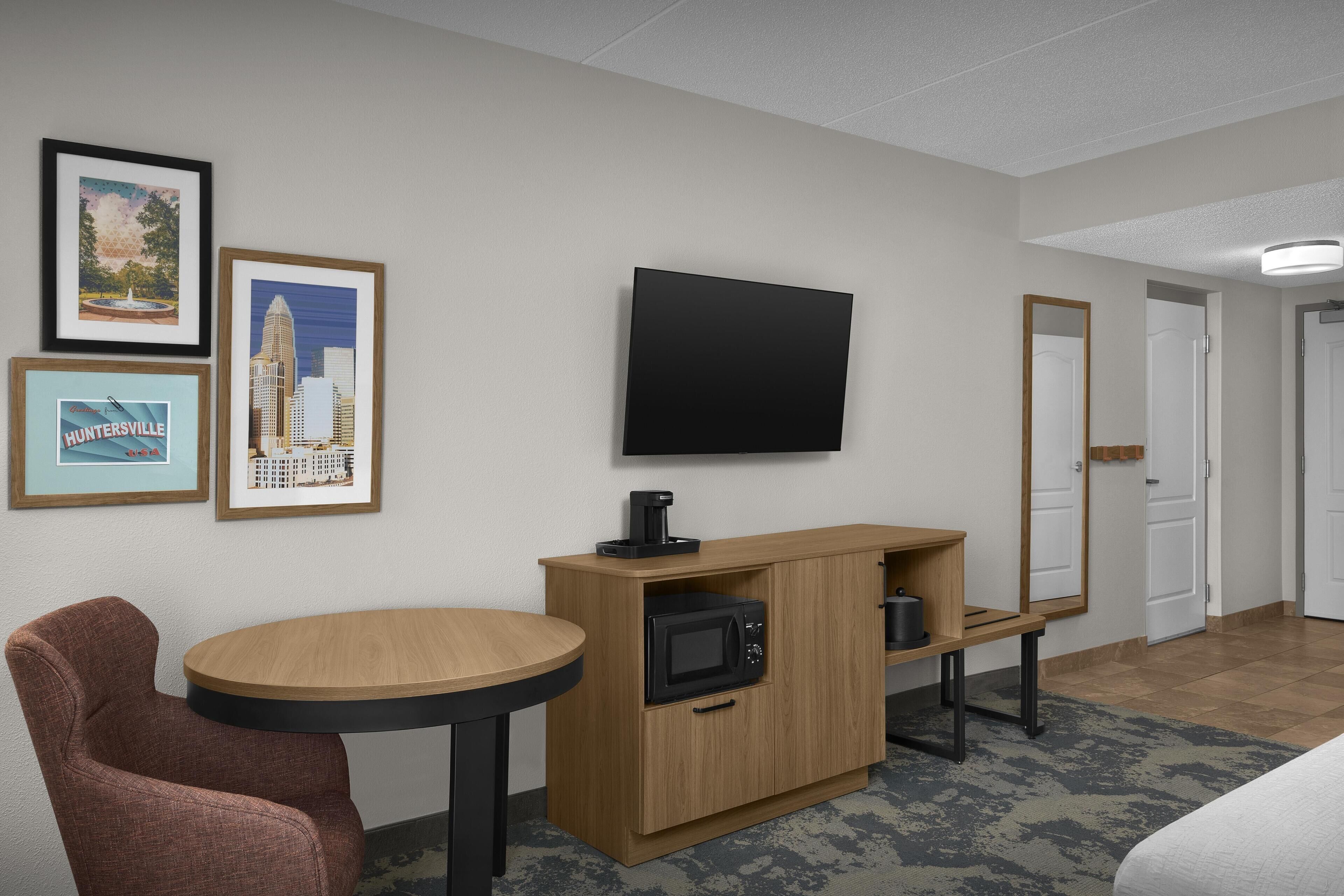 Habitación de hotel con un armario de madera, microondas, televisor de pantalla plana y cuadros en la pared.
