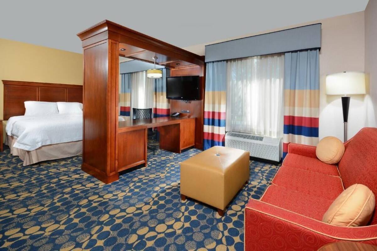 A hotel room with a bed, a desk with a TV, a sofa, and a patterned carpet.