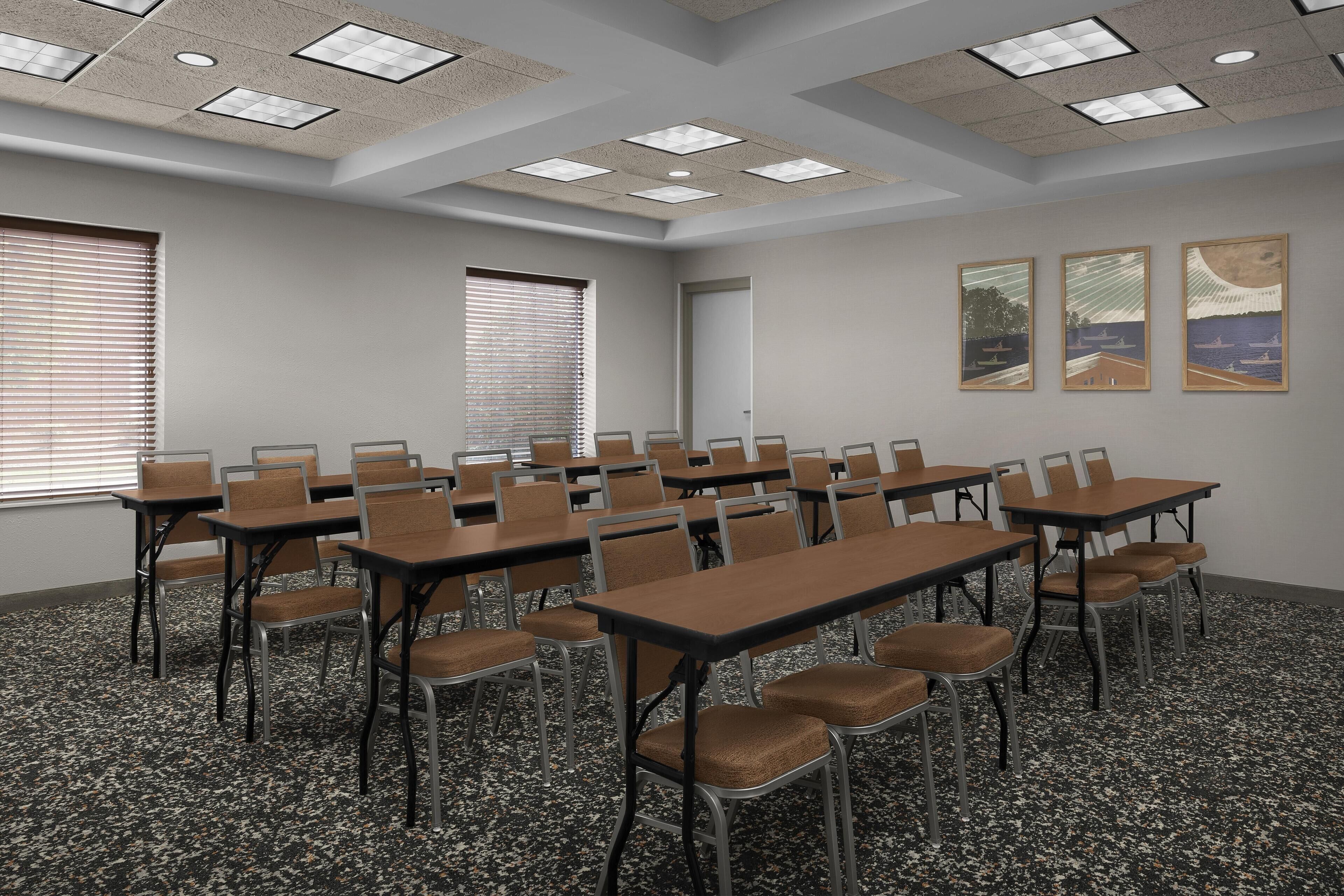 A conference room with tables and chairs, a ceiling with recessed lighting, and three framed artworks on the wall.