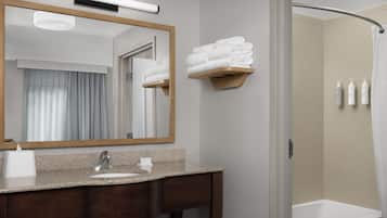A bathroom with a vanity, a mirror, a towel rack, and a shower area.