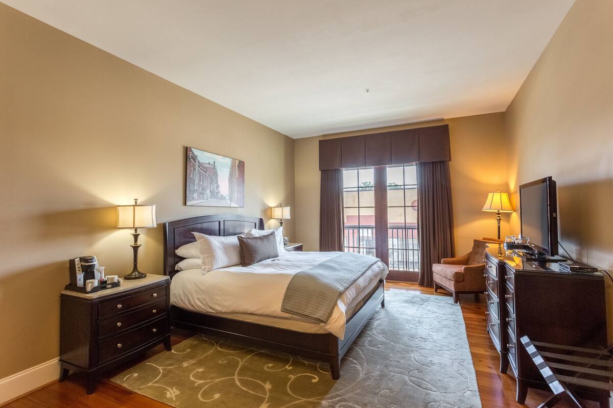 A hotel room with a bed, a desk, a TV, and a window with curtains.