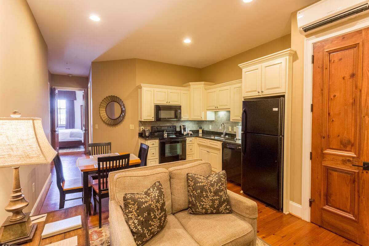 A compact living space with a kitchenette, a sofa with patterned cushions, a dining table, and a lamp.