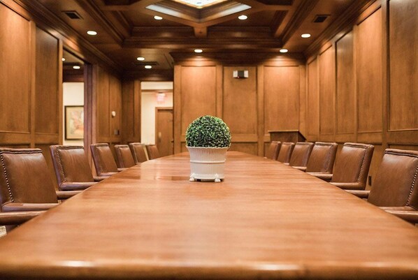 A conference room with a long wooden table, leather chairs, and a potted plant in the center.